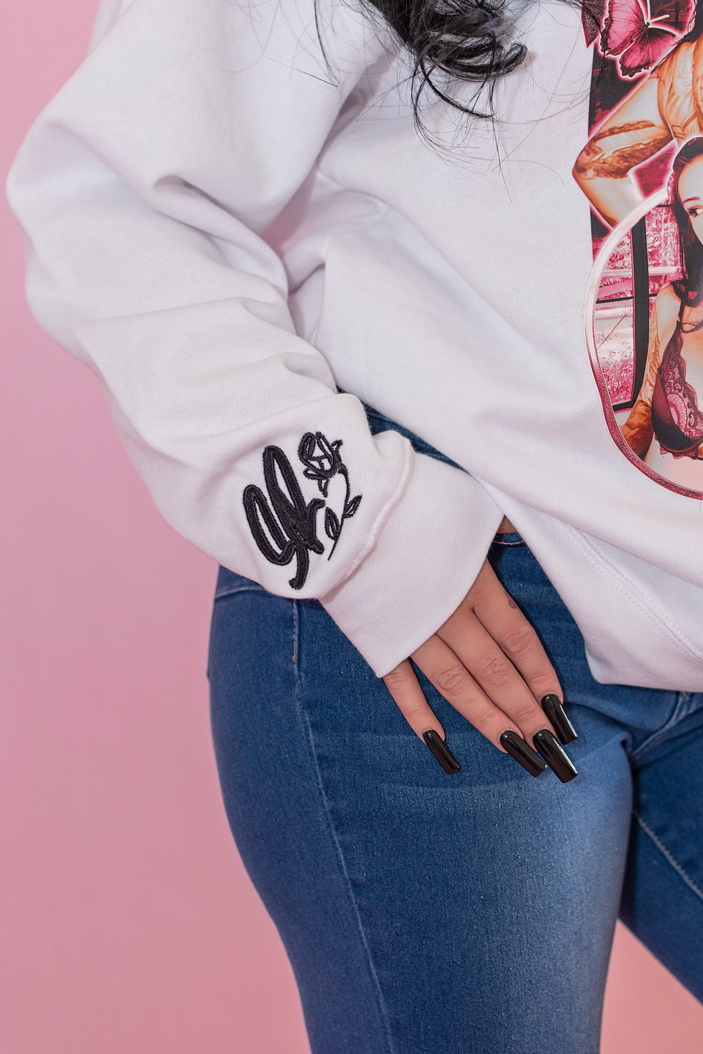 Person wearing a white sweatshirt with a graphic design on a pink background