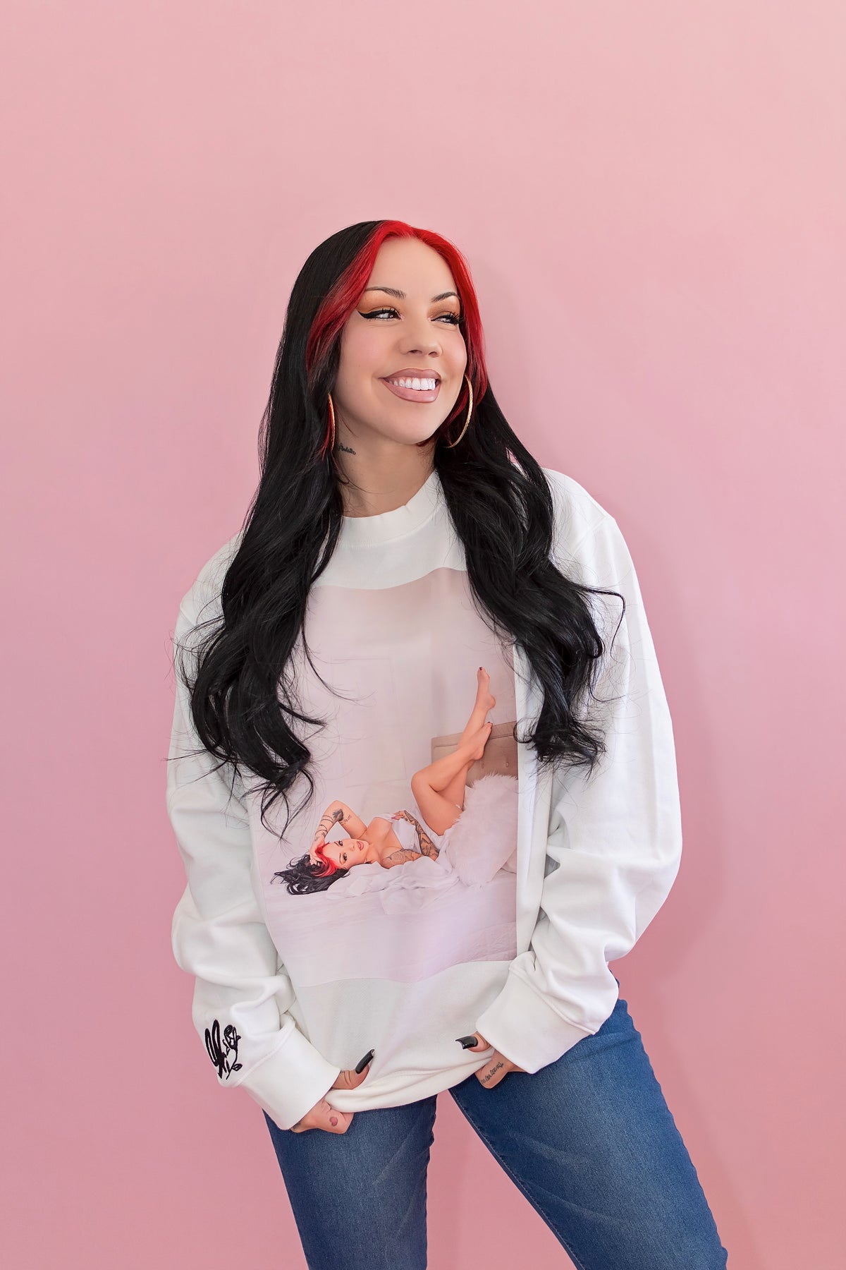 Woman wearing a white sweatshirt with a graphic design on a pink background
