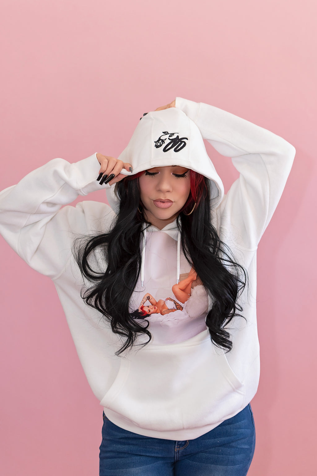 Person wearing a white hoodie with a graphic design on a pink background