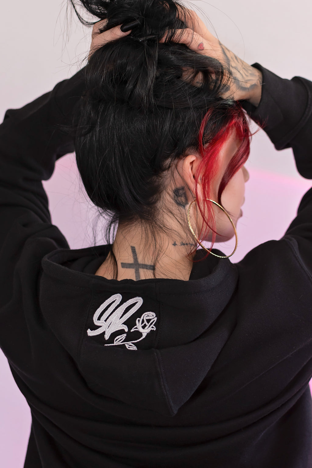 Person wearing a black hoodie with a logo on the back against a pink background