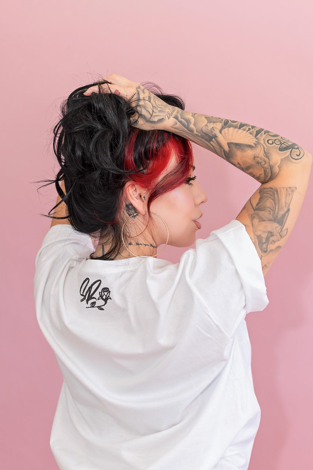Person with tattoos and red hair wearing a white t-shirt against a pink background