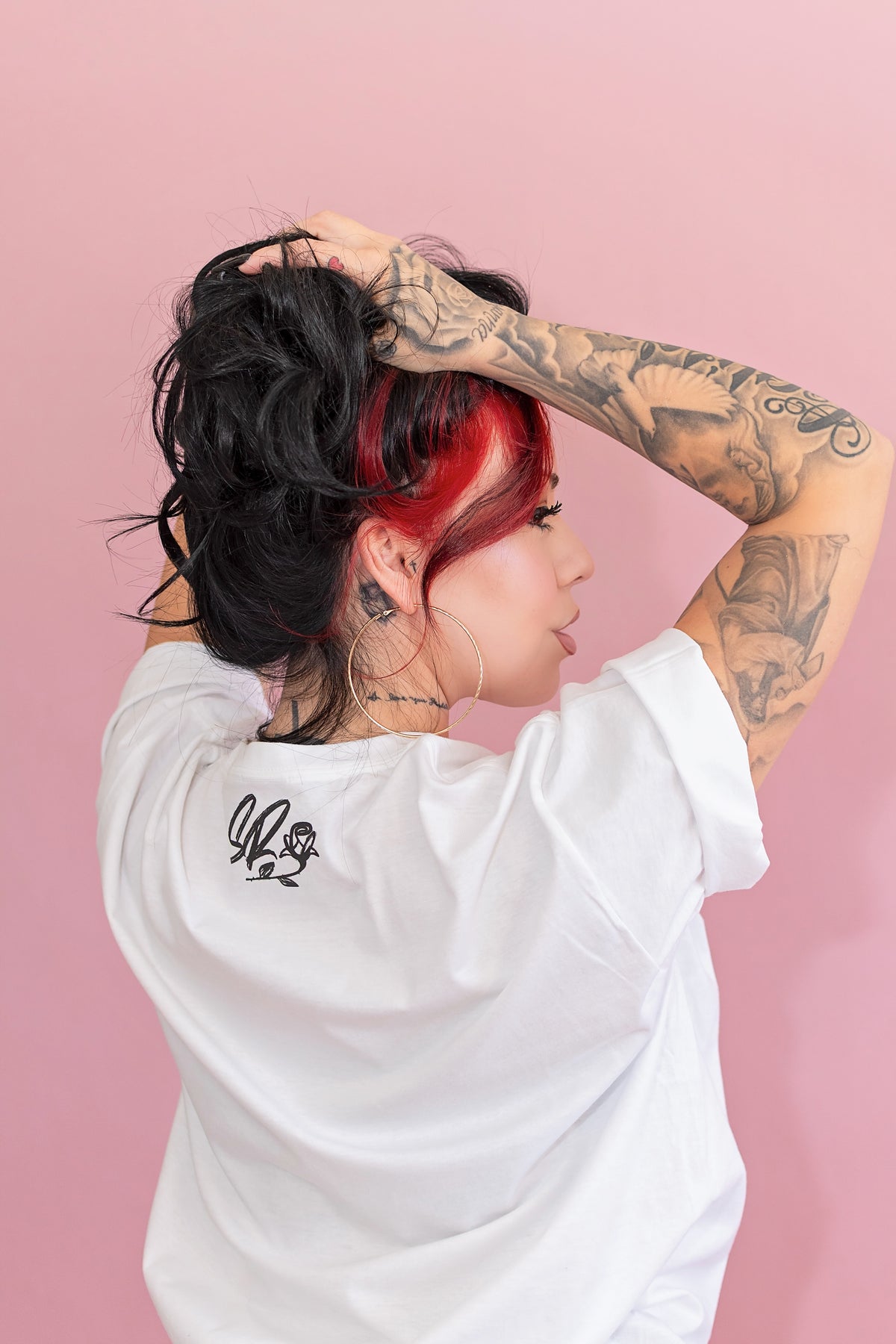 Person with tattoos and red hair wearing a white t-shirt against a pink background